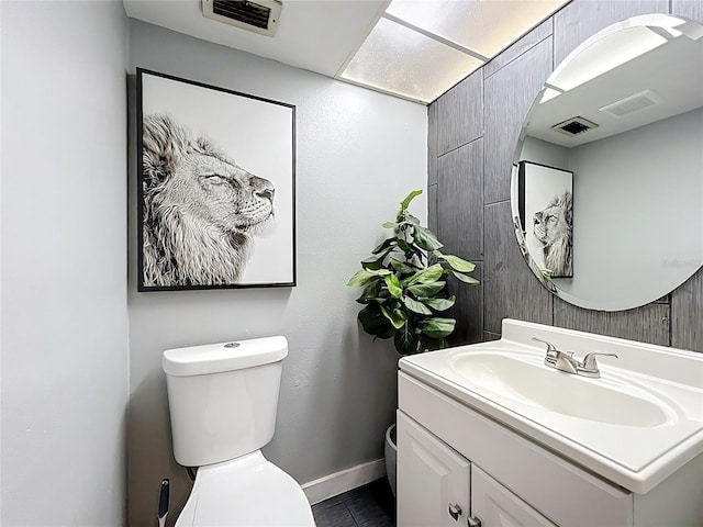 half bathroom with visible vents, toilet, vanity, and baseboards