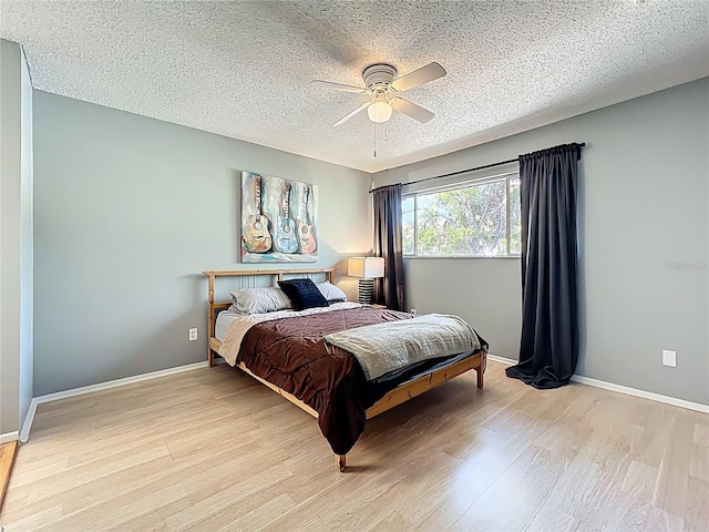 bedroom featuring baseboards, light wood-style floors, a ceiling fan, and a textured ceiling