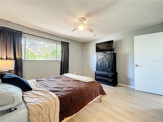 bedroom featuring baseboards, light wood-style flooring, a textured ceiling, and ceiling fan