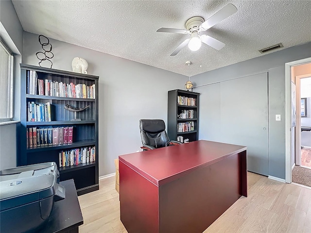 office space featuring light wood finished floors, visible vents, baseboards, a textured ceiling, and a ceiling fan