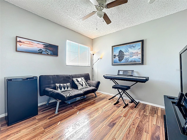 living area featuring ceiling fan, a textured ceiling, baseboards, and wood finished floors