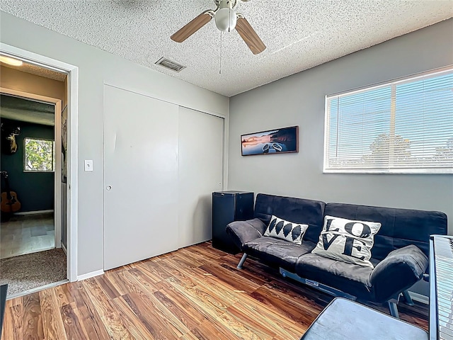 living area with a ceiling fan, wood finished floors, visible vents, and a textured ceiling