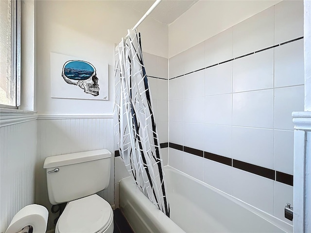 full bath featuring a wainscoted wall, shower / bath combo with shower curtain, and toilet