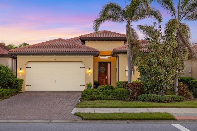 mediterranean / spanish-style house featuring stucco siding, an attached garage, a tile roof, and decorative driveway