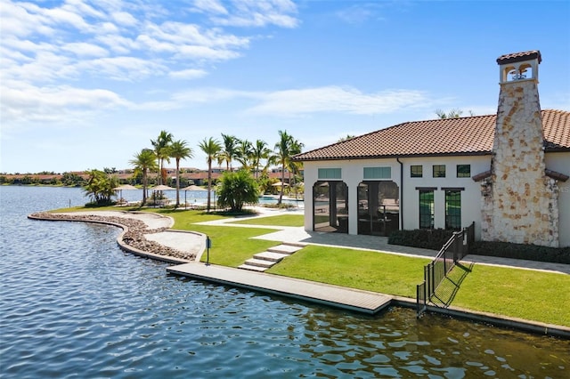 rear view of property with a tiled roof, a lawn, a water view, and stucco siding