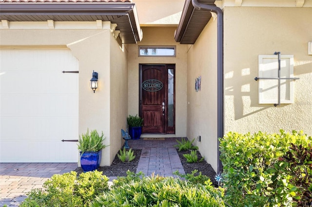 view of exterior entry featuring stucco siding, decorative driveway, and a garage