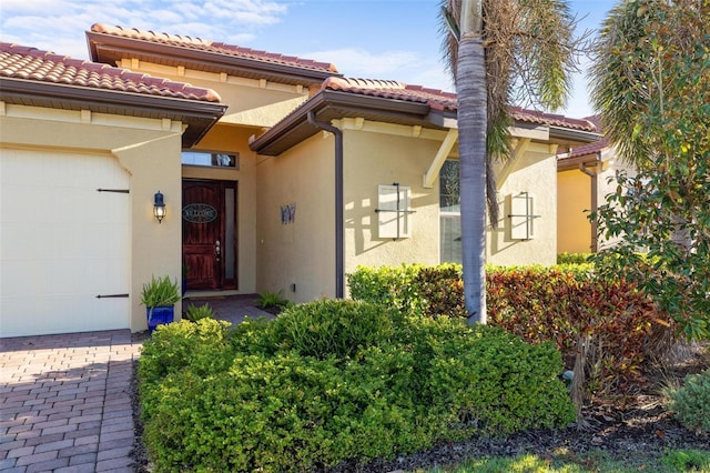 entrance to property featuring decorative driveway, a tiled roof, an attached garage, and stucco siding