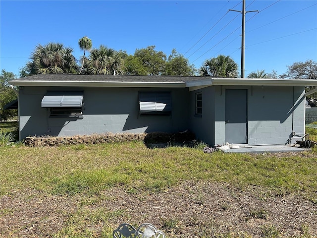 rear view of property featuring a lawn, concrete block siding, and a shingled roof