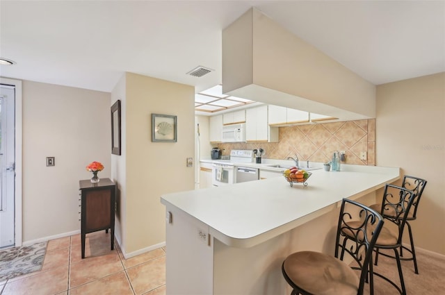 kitchen with tasteful backsplash, light countertops, a kitchen breakfast bar, white cabinets, and white appliances