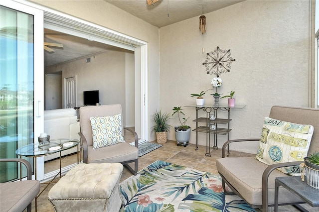 sitting room with a textured wall, visible vents, and ceiling fan