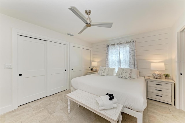 bedroom featuring wooden walls, visible vents, two closets, and ceiling fan