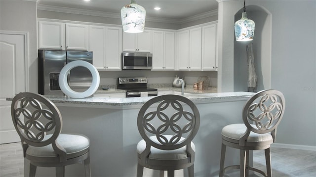 kitchen with stainless steel appliances, a kitchen breakfast bar, ornamental molding, and white cabinets