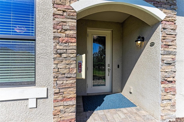 view of exterior entry featuring stone siding and stucco siding