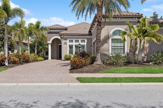 mediterranean / spanish-style home featuring stucco siding, decorative driveway, and a tile roof