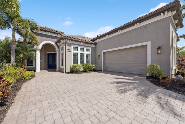 mediterranean / spanish home featuring stucco siding, decorative driveway, and a garage