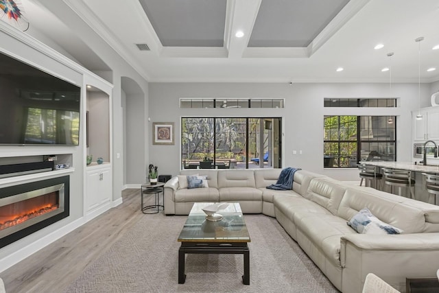 living room with light wood-type flooring, visible vents, ornamental molding, a glass covered fireplace, and recessed lighting