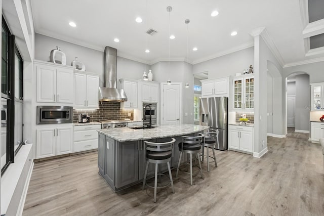 kitchen featuring a center island with sink, visible vents, arched walkways, appliances with stainless steel finishes, and wall chimney range hood