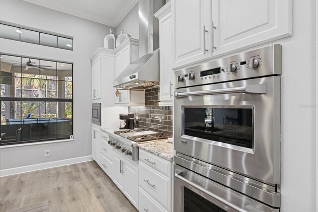 kitchen with decorative backsplash, appliances with stainless steel finishes, white cabinetry, wall chimney exhaust hood, and a ceiling fan