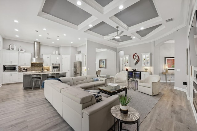 living room with crown molding, a high ceiling, visible vents, and arched walkways