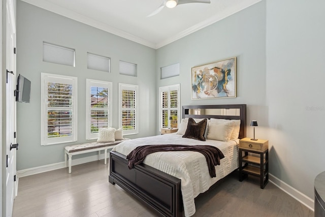 bedroom with a ceiling fan, wood finished floors, a high ceiling, crown molding, and baseboards