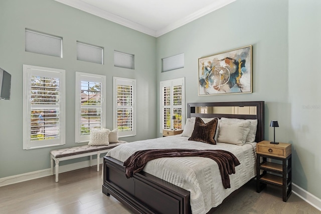 bedroom featuring baseboards, a high ceiling, wood finished floors, and crown molding