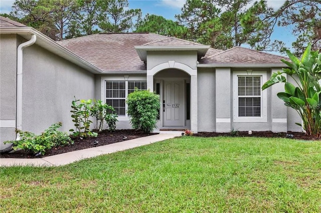 doorway to property with stucco siding, a lawn, and a shingled roof