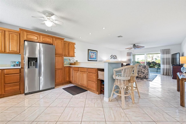 kitchen with visible vents, a peninsula, stainless steel fridge with ice dispenser, light countertops, and a kitchen bar