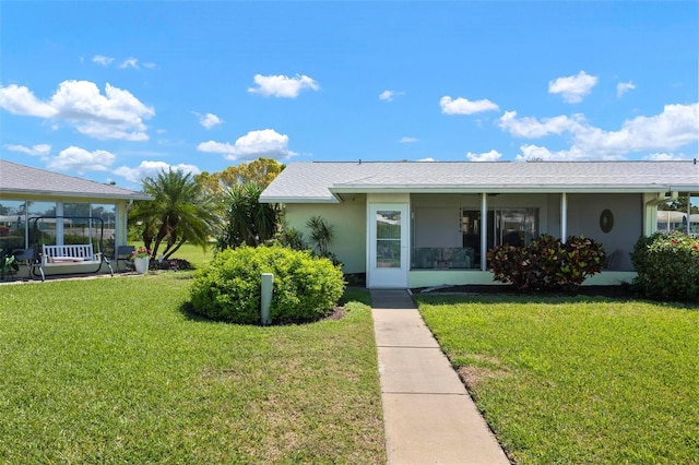 view of front facade with a front yard, a sunroom, and stucco siding