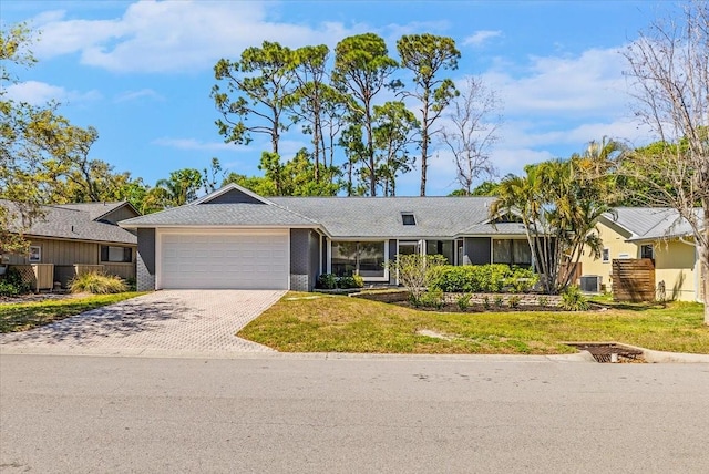 ranch-style house featuring decorative driveway, a garage, central AC, and a front yard