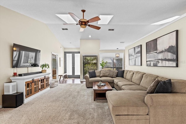 carpeted living area featuring lofted ceiling with skylight, french doors, visible vents, and ceiling fan