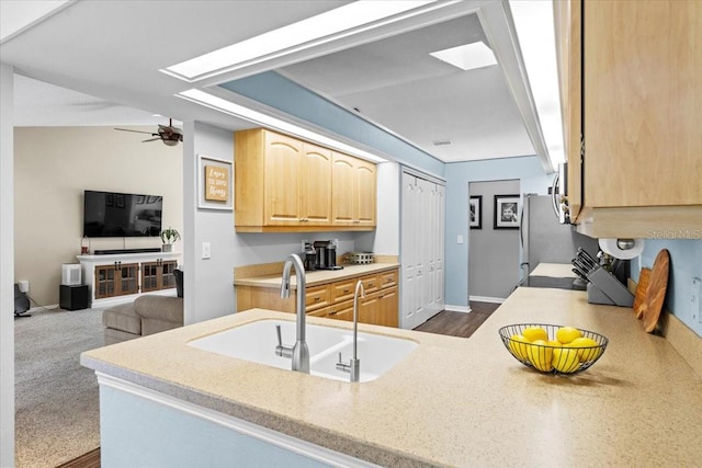 kitchen featuring a ceiling fan, light brown cabinets, a sink, open floor plan, and baseboards