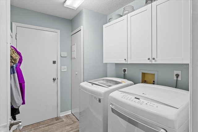 laundry room featuring a textured ceiling, light wood-style flooring, cabinet space, and washing machine and clothes dryer