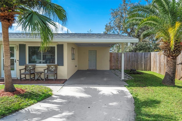 property entrance with an attached carport, fence, driveway, a yard, and stucco siding