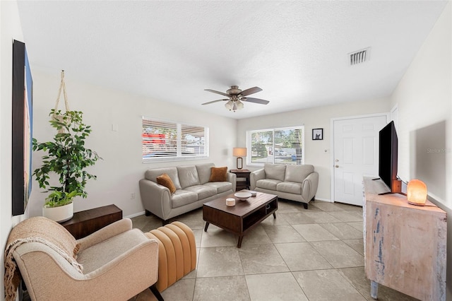 living area featuring light tile patterned floors, visible vents, a textured ceiling, and baseboards