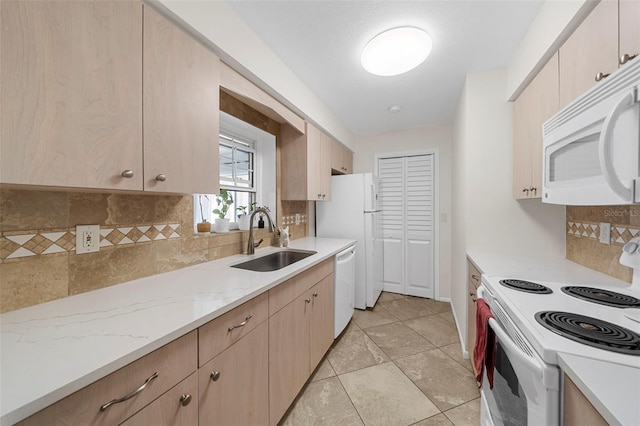 kitchen featuring white appliances, light stone countertops, light brown cabinets, a sink, and tasteful backsplash