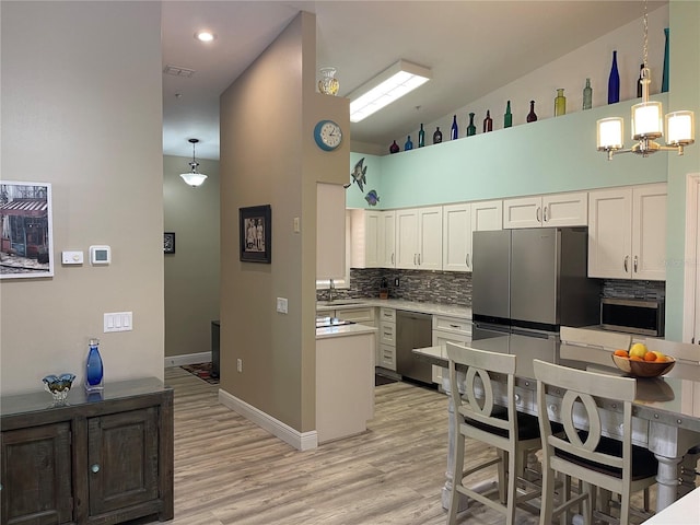 kitchen with tasteful backsplash, light wood-style flooring, appliances with stainless steel finishes, white cabinets, and a sink