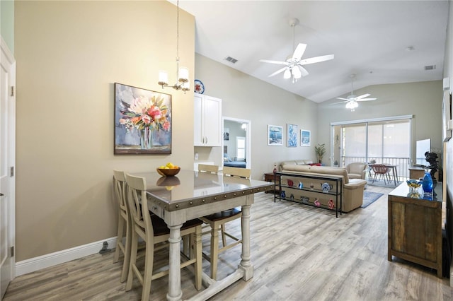 dining room with visible vents, ceiling fan with notable chandelier, baseboards, light wood-style floors, and lofted ceiling