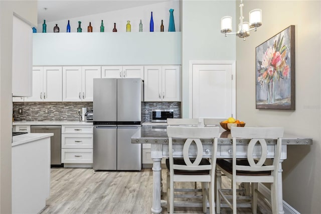 kitchen with tasteful backsplash, appliances with stainless steel finishes, light countertops, and white cabinetry