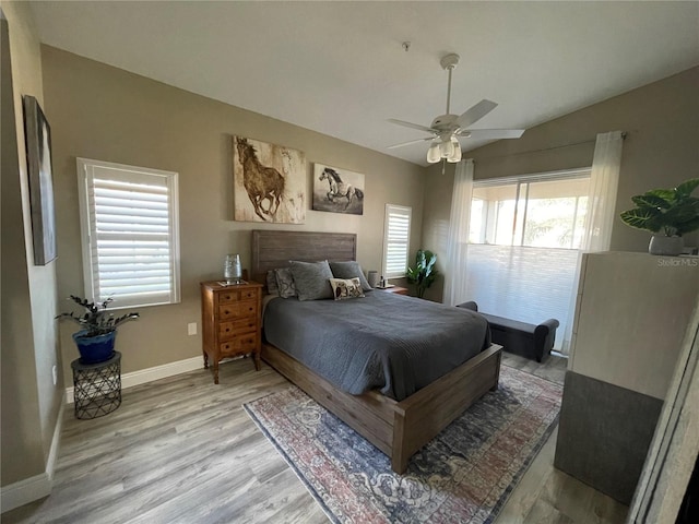 bedroom featuring vaulted ceiling, multiple windows, light wood-style floors, and baseboards