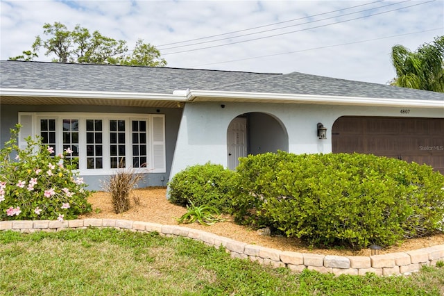 view of exterior entry featuring stucco siding, a garage, and a shingled roof