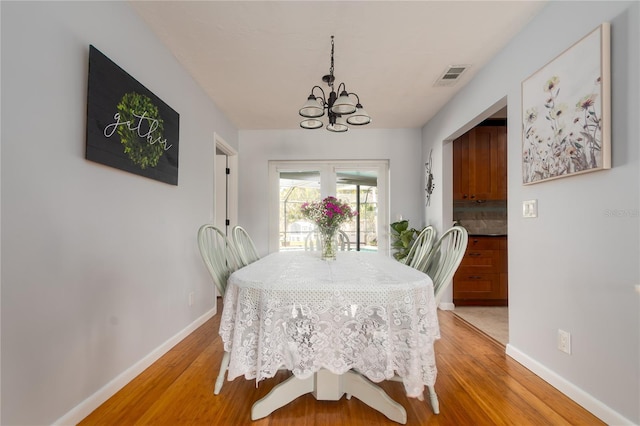 dining space with an inviting chandelier, light wood-style flooring, baseboards, and visible vents