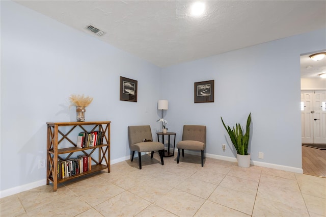 living area featuring light tile patterned floors, visible vents, baseboards, and a textured ceiling