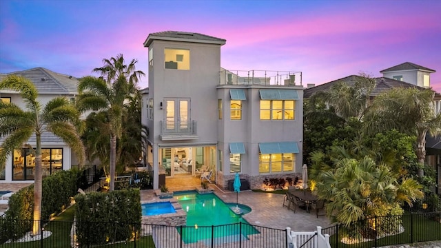 back of house at dusk with stucco siding, a patio, a fenced in pool, a balcony, and fence private yard