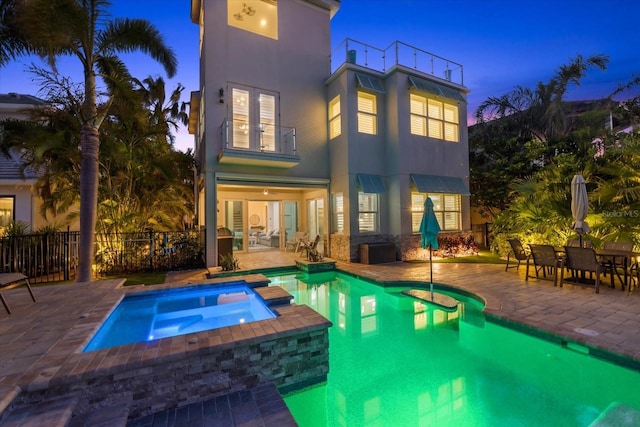 back of house at dusk with a patio, a balcony, fence, stucco siding, and french doors