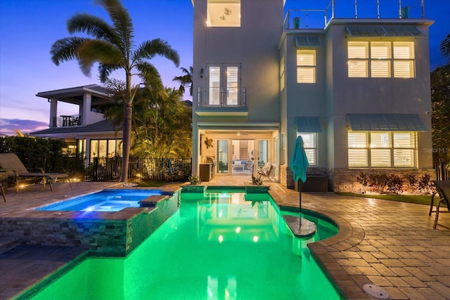 back of house at dusk with a patio, a balcony, french doors, and stucco siding