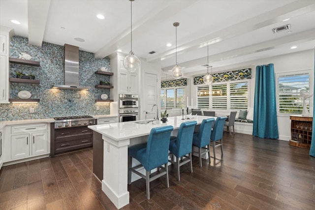 kitchen featuring open shelves, stainless steel appliances, light countertops, beamed ceiling, and wall chimney exhaust hood