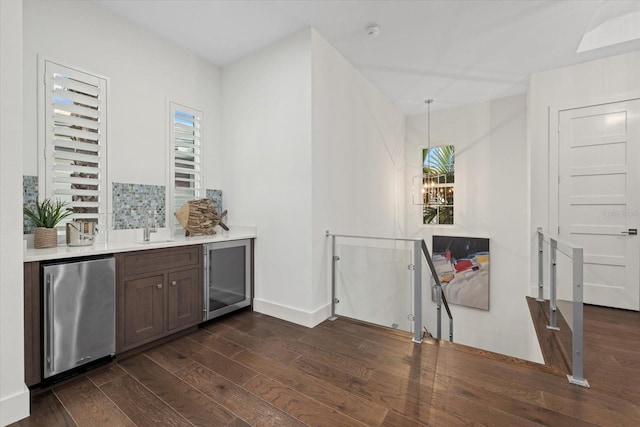 bar featuring a sink, dark wood-style floors, stainless steel fridge, and baseboards