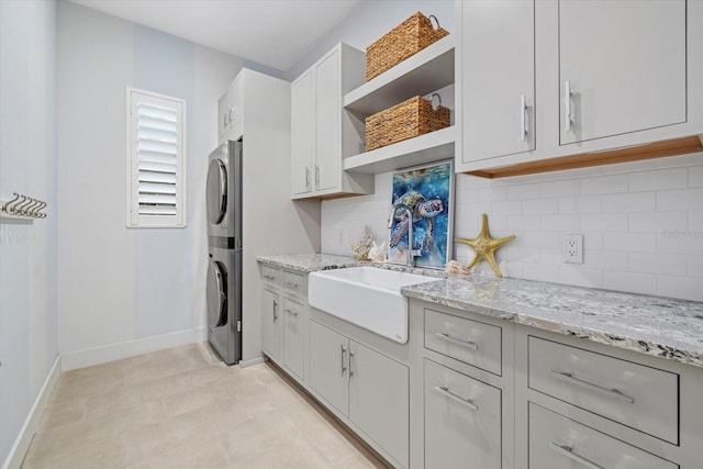 kitchen with backsplash, open shelves, light stone countertops, stacked washing maching and dryer, and a sink