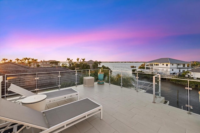 patio terrace at dusk featuring a water view and a balcony