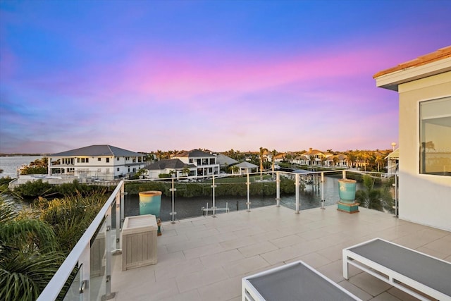 patio terrace at dusk featuring a residential view, a balcony, and a water view